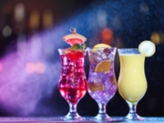 Glasses of alcoholic cocktails with garnish on table against blurred background with smoke