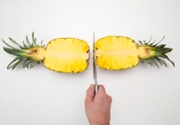 Pineapple sliced in two lengthwise lying against white backdrop with knife.