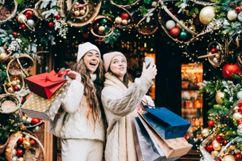 Two long-distance girl friends enjoying their holiday reunion during European Christmas and New Year December celebrations, taking a selfie with funny faces for their friends during their Secret Santa shopping and preparations. Togetherness and bonding, fostering relationships and friendship. Christmas shopping and holiday offers concept
