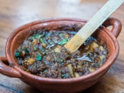 A small terracotta bowl with wooden spoon with Mexican charred salsa verde on a restaurant table in Playa del Carmen