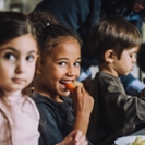 Happy girl eating carrot for breakfast with classmates in kindergarten