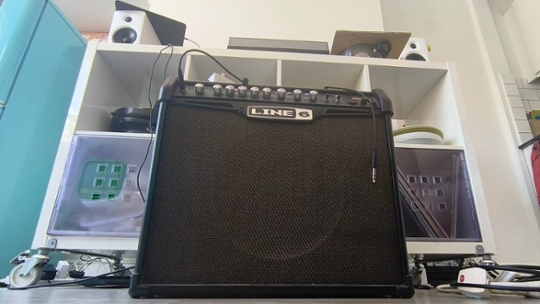guitar amp in front of a white storage unit containing hi-fi equipment