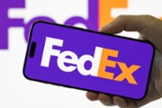 CHONGQING, CHINA - SEPTEMBER 14: In this photo illustration, a smartphone held in a hand shows the logo of FedEx Corp. (NYSE: FDX), a U.S. multinational courier delivery services company providing express transportation, e-commerce and business services, with the company's logo enlarged in the background on September 14, 2025 in Chongqing, China. (Photo illustration by Cheng Xin/Getty Images)